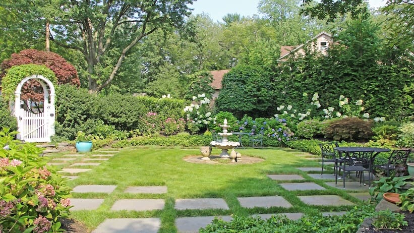 Renovated New Jersey garden with a curved walkway, colorful plantings, and mature trees.
